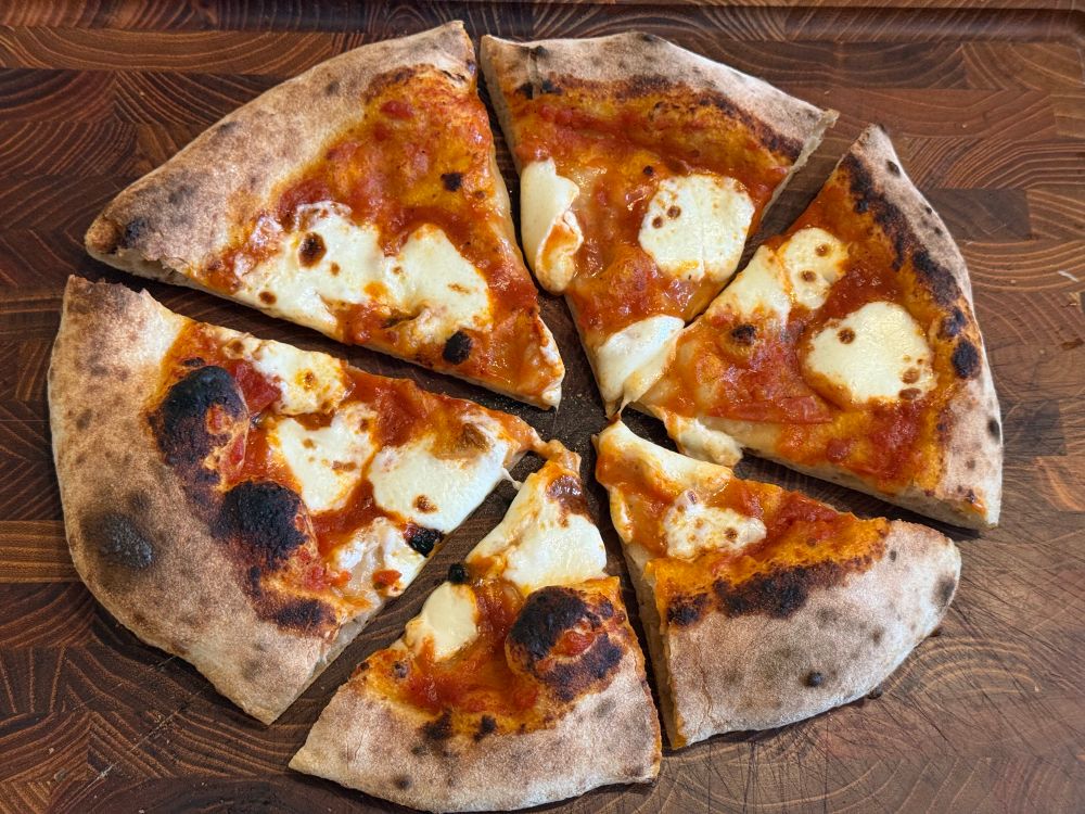 Fresh mozz pizza cut in six slices in a wood cutting board 
