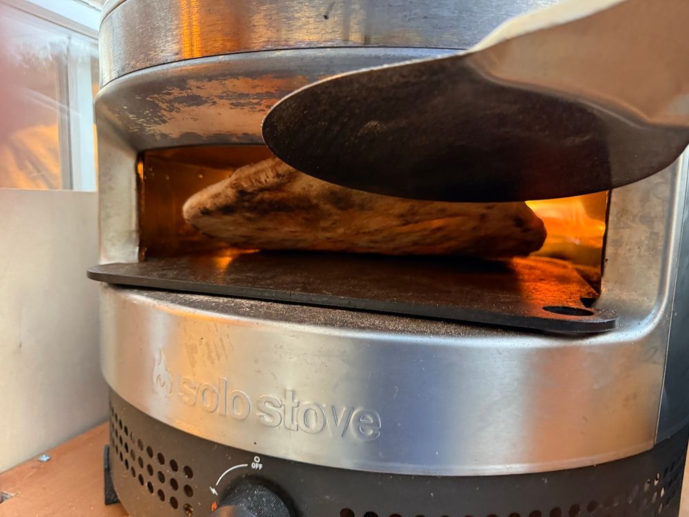 A pizza in a pizza oven being lifted up so you can see the perfectly-cooked bottom