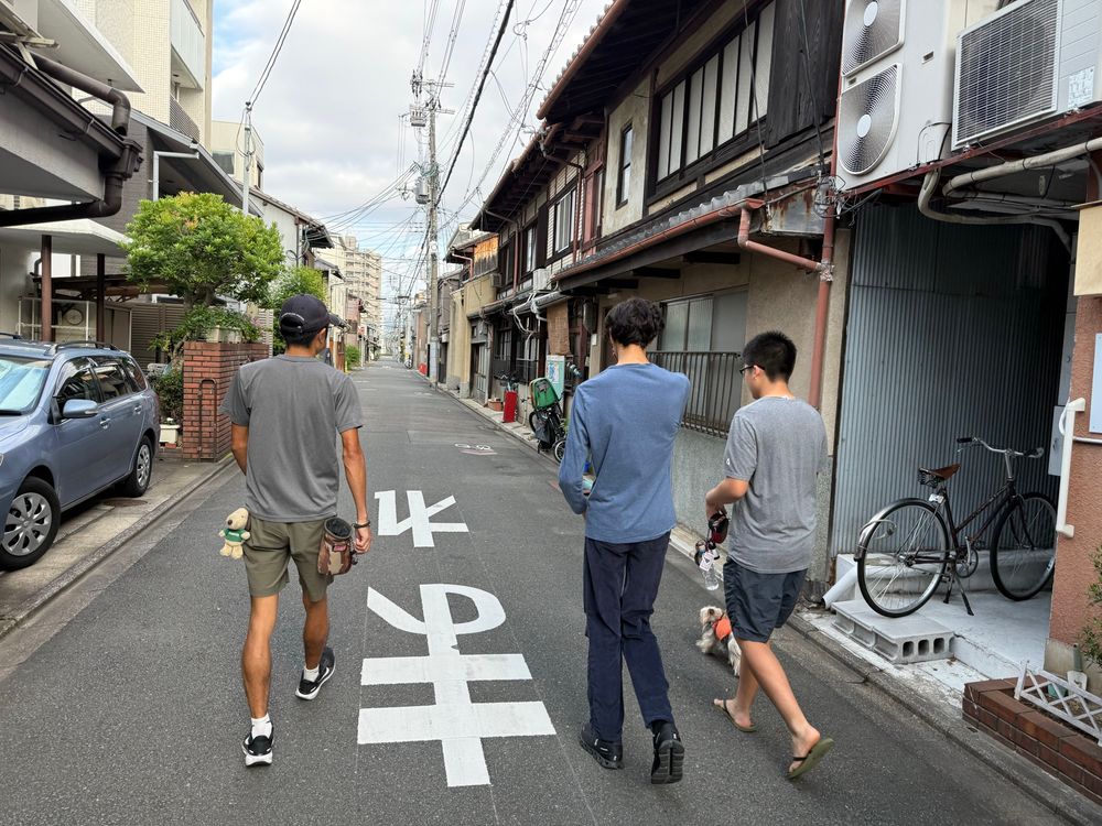 Three people walking a dog on a Kyoto street 