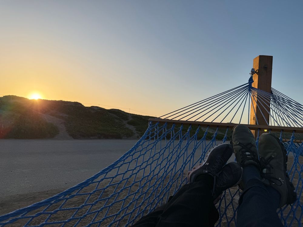 Two people laying in a hammock (only their legs are visible), watching a sunset at the new Sunset Dunes park