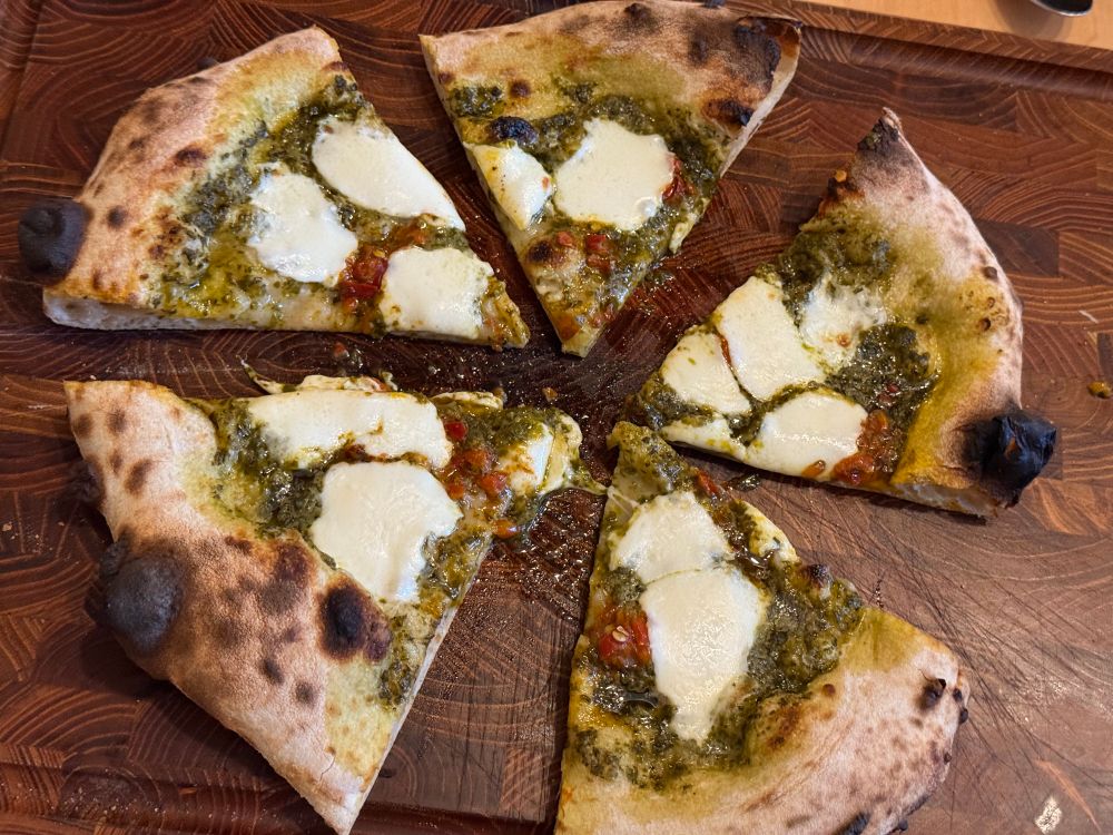Pesto, Calabrian pepper, and fresh mozz pizza on a wood cutting board 