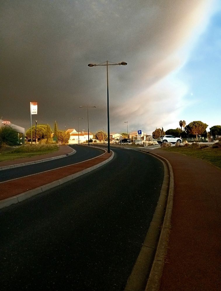 Une route avec des bandes colorées et un ciel partagé sombre d’un côté et bleu de l’autre.