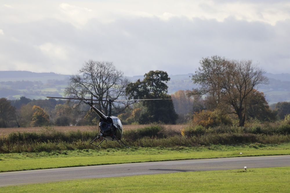 Small helicopter taking off along runway gaining altitude and speed.