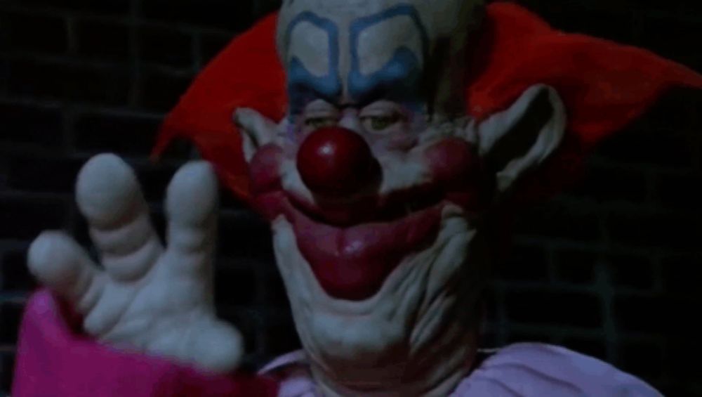 a clown with a red nose is waving his hand in the dark