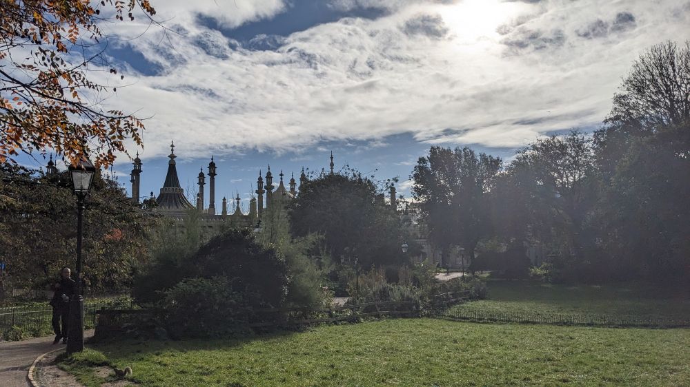 A photo of Brighton pavilion taken from the pavilion gardens in bright sunshine. The pavilion spires are visible above the trees of the gardens.