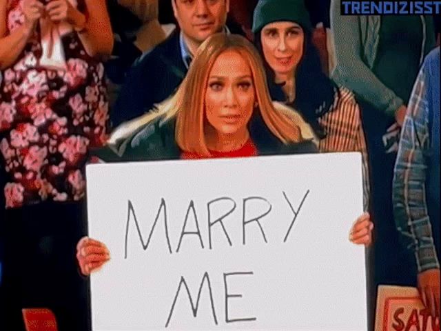 a woman in a crowd holds up a sign that says marry me