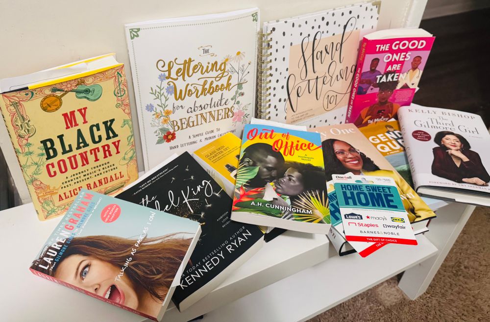 A display of various books from Brit’s tenure wish list. It features “My Black Country,” “talking as fast as I can” “out of office” various calligraphy lettering books, “the third Gilmore girl” “out of office,” etc. 