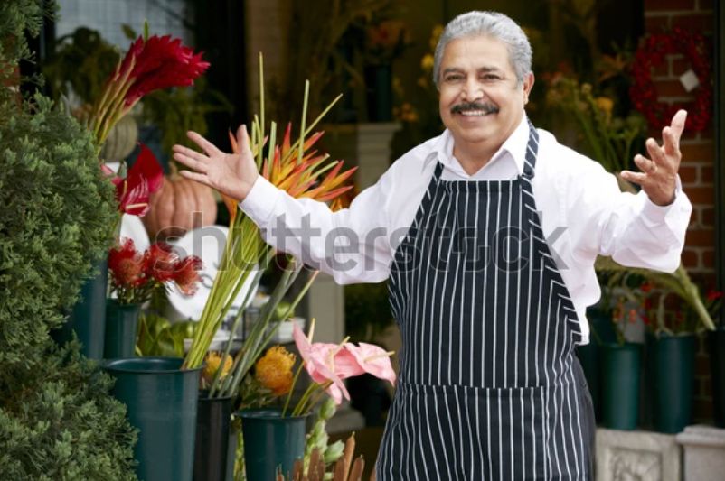 A watermarked stock photo of an older Italian gentleman in an apron, a shop owner of some kind, stepping up with a smile and his arms open in greeting. It’s the same picture every day. Today he is getting over the sniffles!