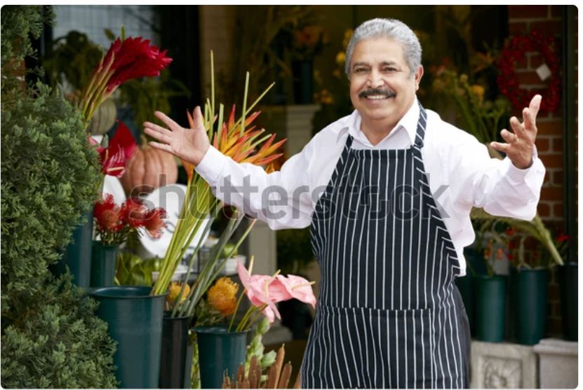 A watermarked stock photo of an older Italian gentleman in an apron, a shop owner of some kind, stepping up with a smile and his arms open in greeting. It’s the same picture every day. Today is so nice he has left the windows open in the shop!