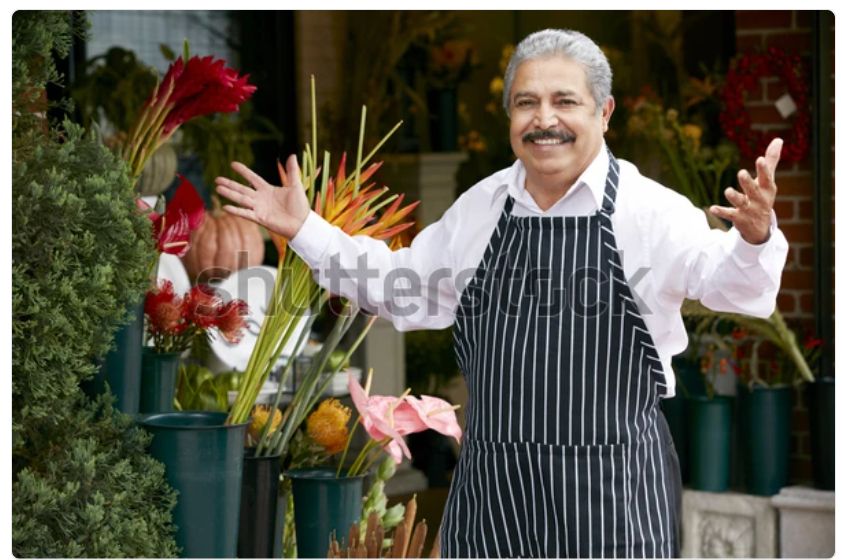 A watermarked stock photo of an older Italian gentleman in an apron, a shop owner of some kind, stepping up with a smile and his arms open in greeting. It’s the same picture every day. Today he has a fresh haircut!