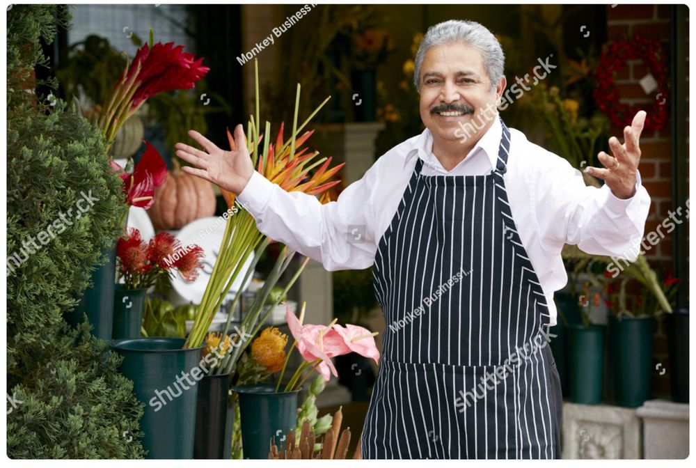 A watermarked stock photo of an older Italian gentleman in an apron, a shop owner of some kind, stepping up with a smile and his arms open in greeting. It’s the same picture every day. Today he is wearing a new apron! It looks like all the other ones.