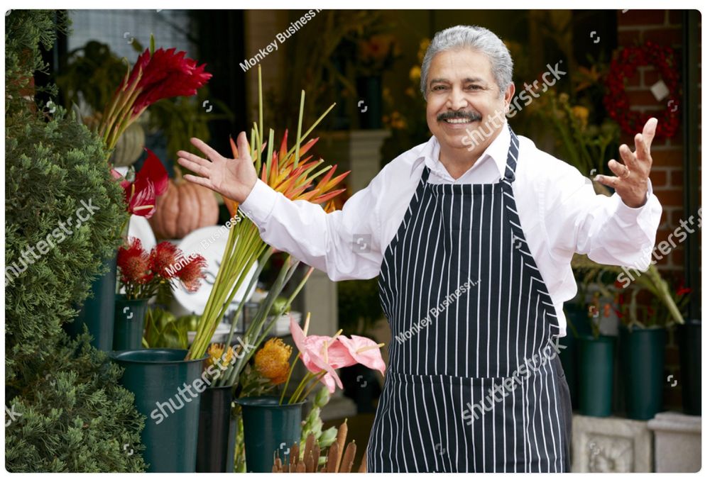 A watermarked stock photo of an older Italian gentleman in an apron, a shop owner of some kind, stepping up with a smile and his arms open in greeting. It’s the same picture every day. Today he is saying "TGIF!"