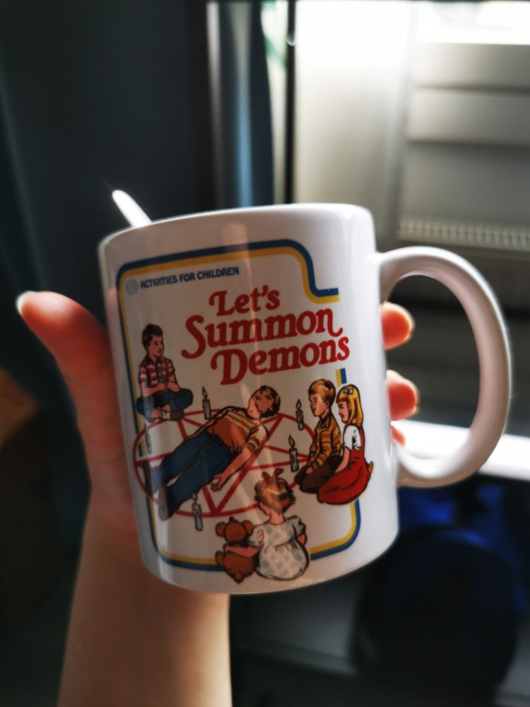 mug that has text that says "let's summon demons". on the side is an illustration of children sitting in a circle around a pentagram where one child lays in the middle of it. 