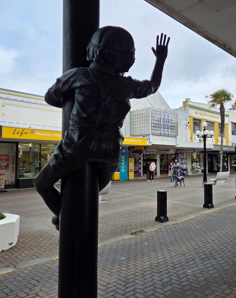 Napier NZ is known for its art deco buildings. A severe earthquake hit, leveling much of the town. When they rebuilt, art deco was popular so there we have it. Nice town with a fairly vibrant shopping/pedestrian area, long waterfront park and of course, close to many wineries. We did take a day trip to where most of the wineries and close to and that place is called Hastings. Next trip time we stay in the area, it will be in Hastings. At LEAST as much to do as in Napier and MUCH more centralized to the majority of wineries. 
The photo is on the main pedestrian area. Kids on the pole is waving to the lady walking the dog. Might have to zoom to see her.