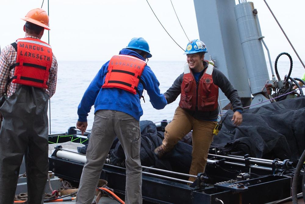 a scientists smiles while stepping over a large net with the help of another scientist