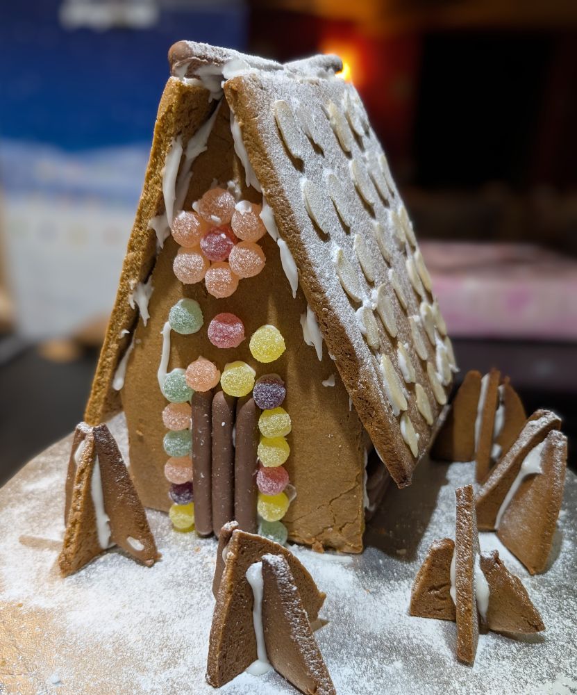 A gingerbread house covered in sweets and chocolate fingers, dusted in icing sugar
