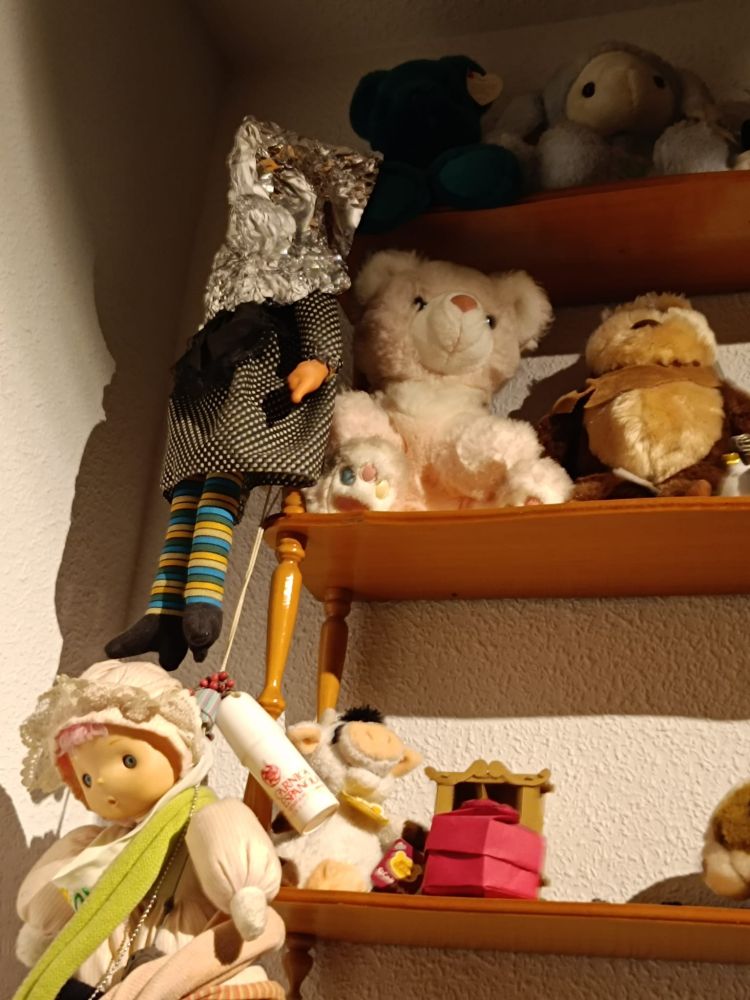 Varios muñecos y peluches en una estantería. Doña Rogelia tiene la cara tapada con papel de aluminio.