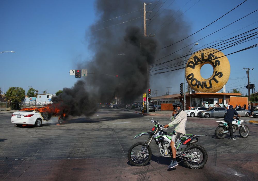 People ride motorbikes next to a car burning in flames during a standoff between police and protesters following multiple detentions by Immigration and Customs Enforcement (ICE), in the Los Angeles County city of Paramount, California, U.S., June 7, 2025 (REUTERS)