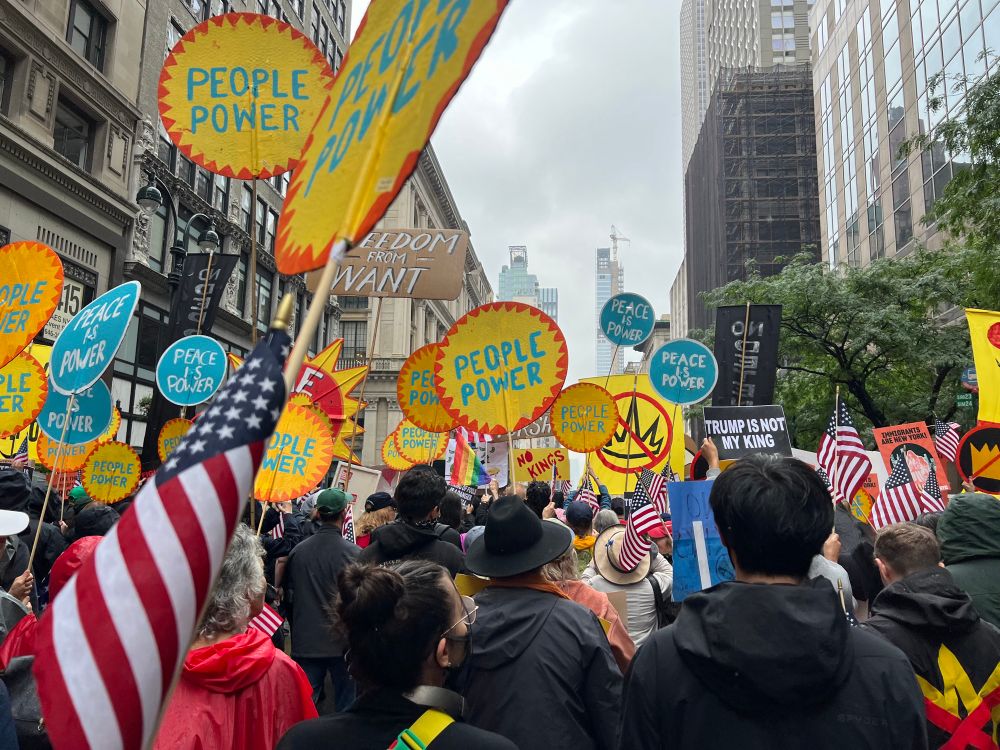 Picture of the crowd with lots of hand painted crowns crossed out (No Kings), People Power, and Peace is Power