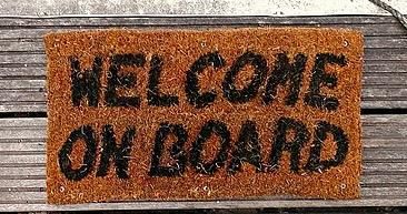 Mabel Amber: Füße in roten Sportschuhen vor Fußmatte mit der Aufschrift "Welcome on Board“, https://commons.wikimedia.org/wiki/File:Welcome_on_Board.jpg, Creative-Commons-Lizenz CC0 1.0
