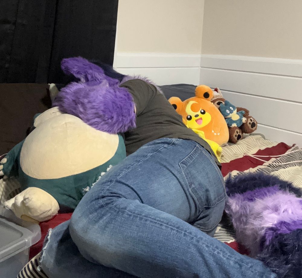 Purple cat fursuiter asleep while holding a Snorlax plushie