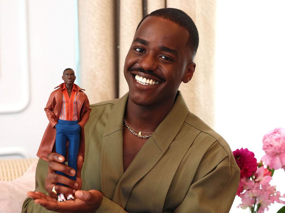 15th Doctor of Doctor Who Ncuti Gatwa holding the Barbie doll made in his image and smiling.