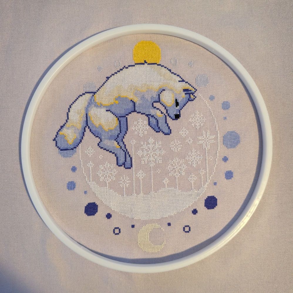 Image of a cross stitched arctic fox leaping into the snow
