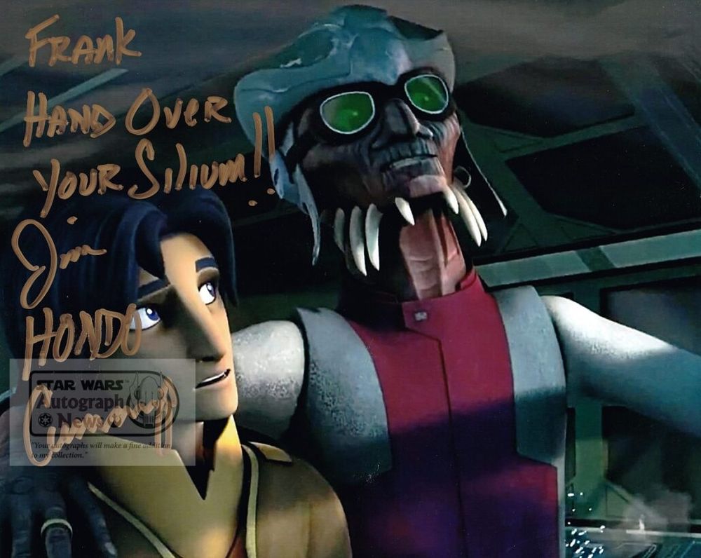 An image of Hondo ohnaka, a spikey faced reptilian pirate known for stabbing everyone. Himself included, in the back, with the Jedi he has decided will be his pirate apprentice, Ezra Bridger, looking unsure and perhaps a bit concerned. There's an autograph in gold over the image - "frank hand over your silium!! - Jim HONDO Cummings" 