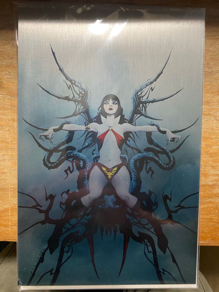 Alt text: Vampirella: Black, White and Blood. This is the metal Jae Lee cover with his signature dark and kind of spiky aesthetic. On it, Vampirella is pictured sitting on what looks like a jagged throne of bones (the seat is not jagged, that part looks comfortable enough). 
