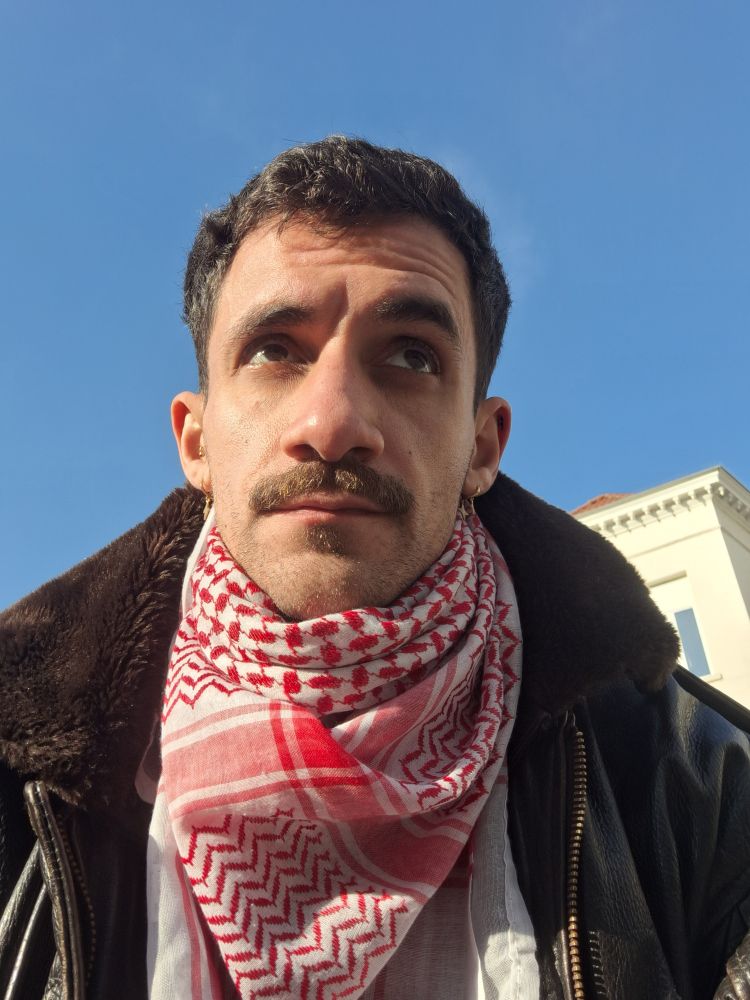 Selfie sur fond de ciel bleu et un keffieh rouge autour du cou.