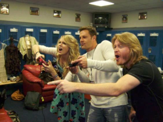 A teenage girl and two men holding game controllers, playing in a high school room