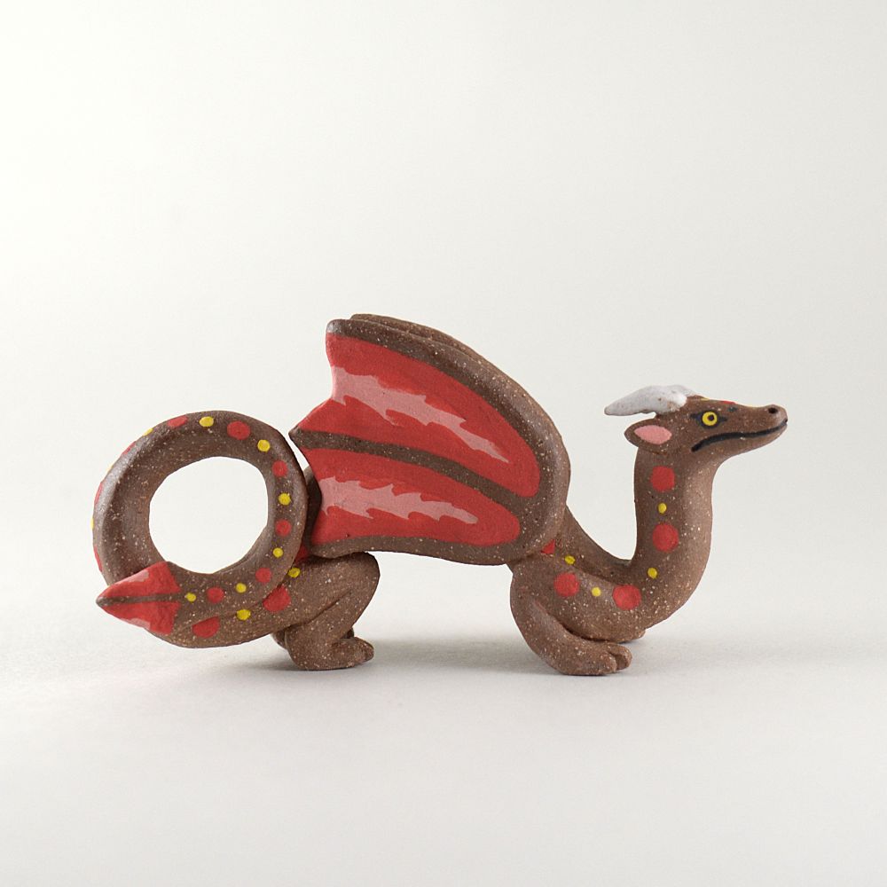 A photo of a ceramic dragon on a white background. The dragon has a brown body with tiny speckles and has red, pink, and yellow details.