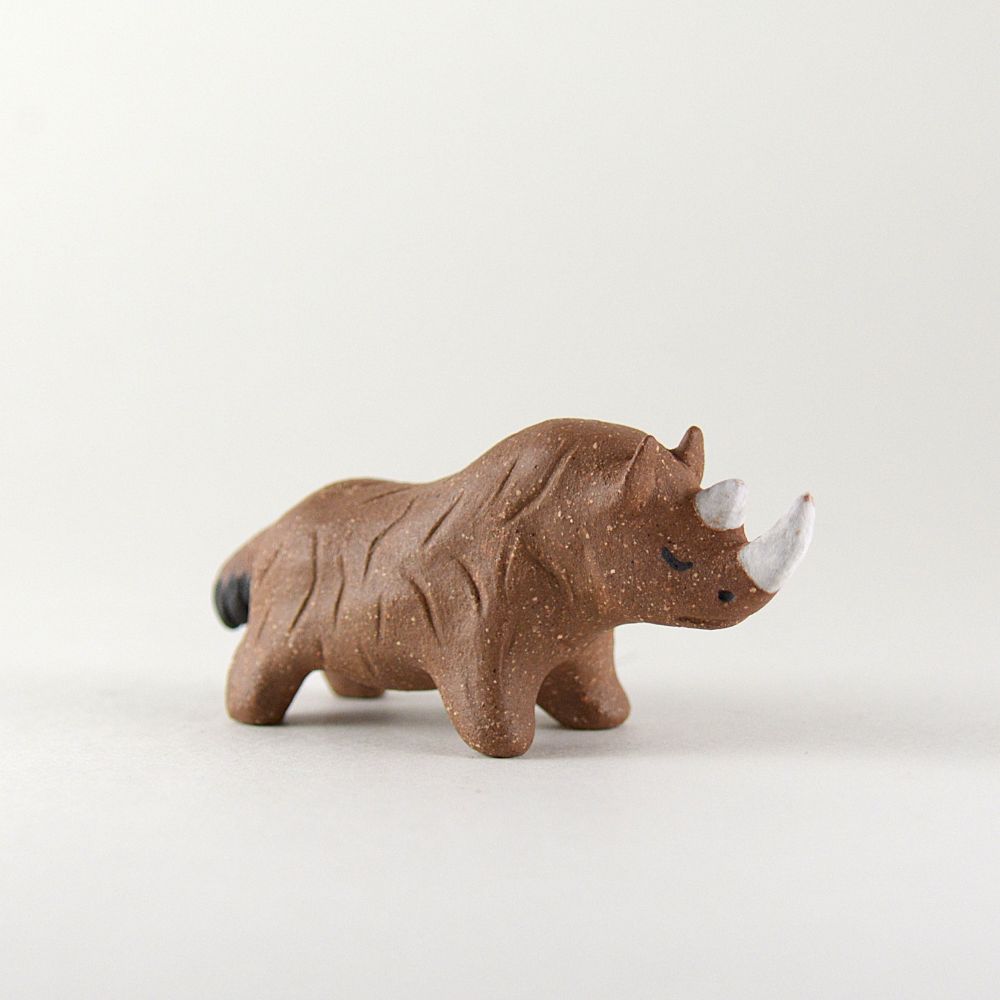 A photo of a little ceramic rhino on a white background. The rhino is made of brown clay with texture to indicate fur.