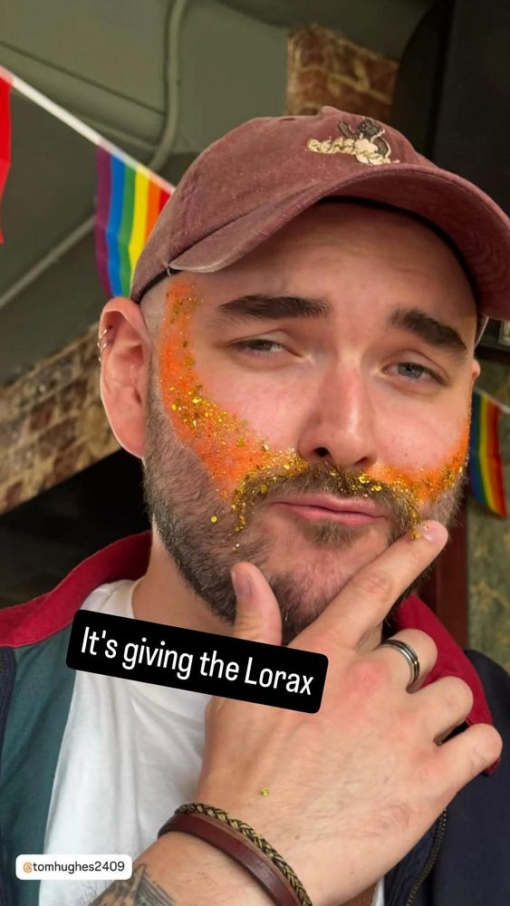 My face with orange face glitter and a gold moustache, caption of "It's giving Lorax"