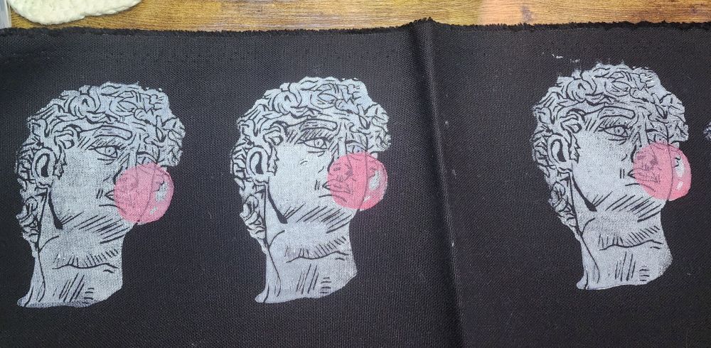 The same David headshot patch in the quoted post but the bubble is now filled in with pink and there are two MORE David heads printed on a strip of black denim
