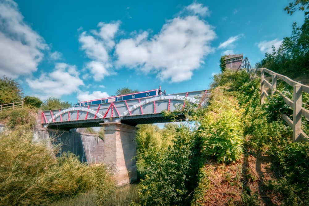 Photo of a narrowboat on an iron-trough aqueduct with grey brick abutments and a central masonry pier. 