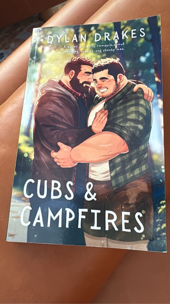 Cover of Cubs & Campfires by Dylan Drakes. Showing two bearish men holding each other in the woods while smiling.