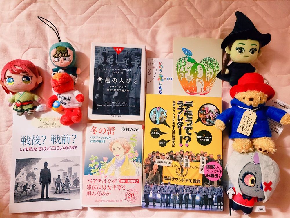 布団の上に本が3冊並べてある。
『増補 普通の人びと ホロコーストと第101警察予備大隊』クリストファー・R・ブラウニング/谷喬夫
『冬の蕾 ベアテ・シロタと女性の権利』樹村みのり
『デモってラブレター!? 福岡サウンドデモ本人訴訟顛末記』
本の左に、
『愛書家の楽園vol.162「戦後？ 戦前？ いま私たちはどこにいるのか」』
というチラシが置かれている。
『デモってラブレター』の上には、いのうえしんぢさんの名刺とイラスト作品のポストカードが置かれている。
さらにその周りに、北原キョウカ、中在家長次、エルモ、エルファバ、パディントン、ヴァギーのぬいが並べてある。