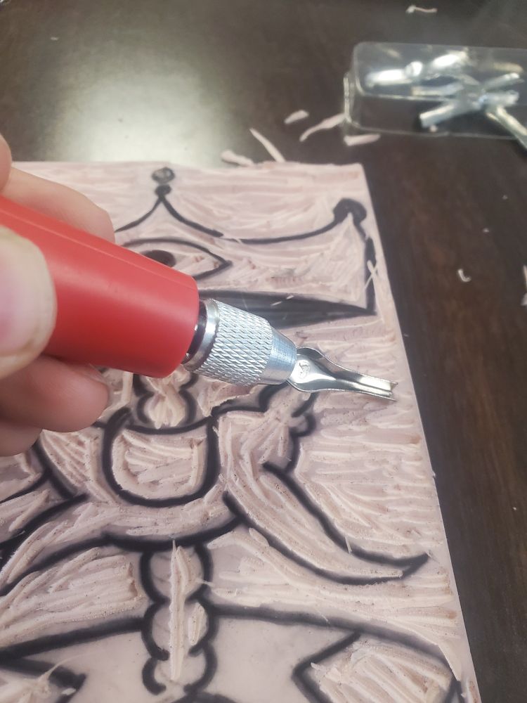 Photo of a linocut block being carved, with a hamd holding a red blade