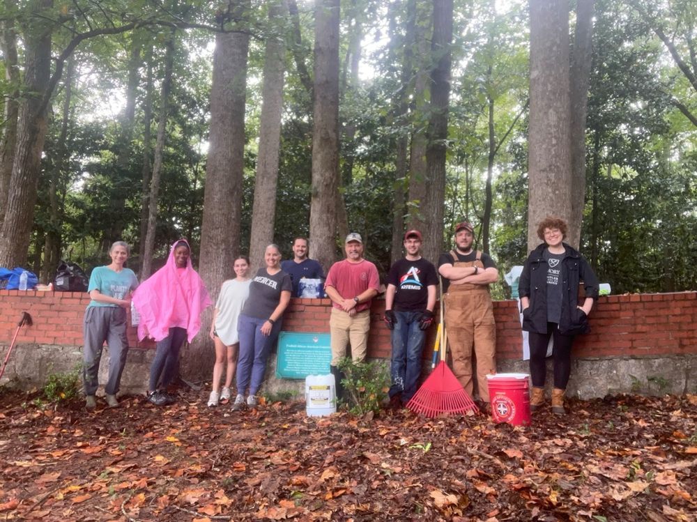 9 volunteers standing along a brick wall outside a historic cemetery