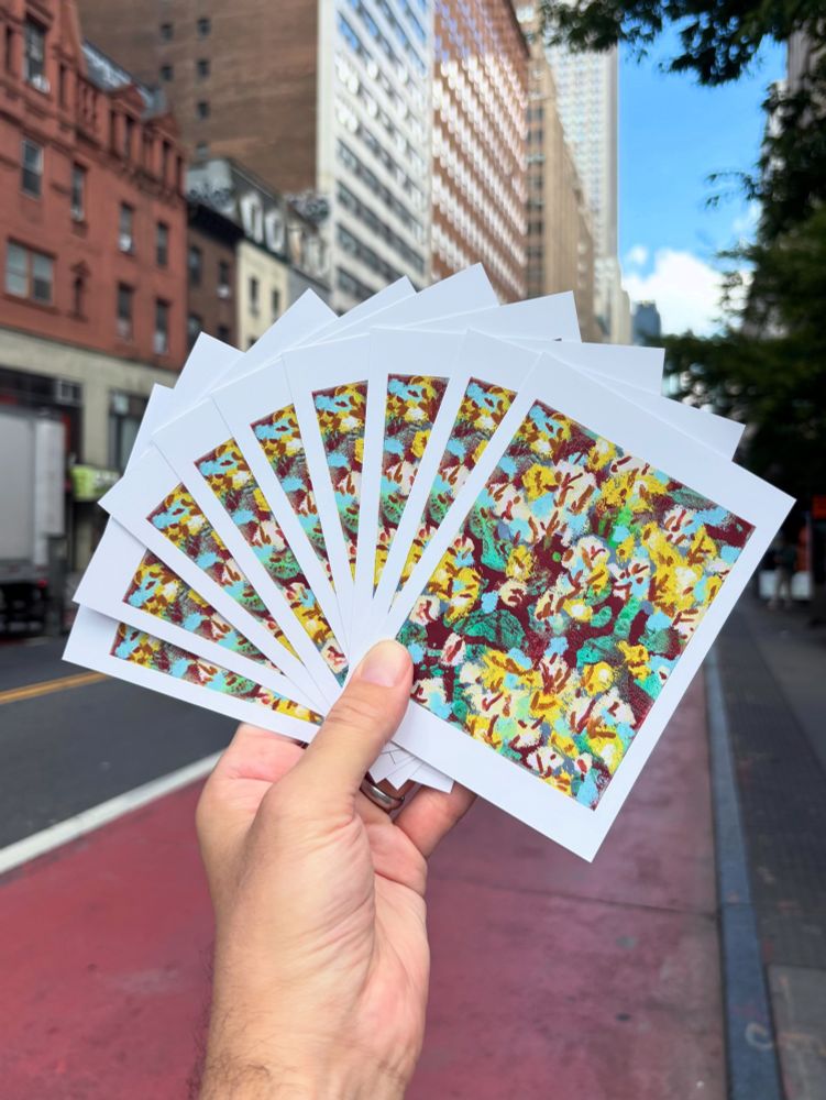 A hand holding up multiple exhibition postcards with a NYC street scene in the background. 
