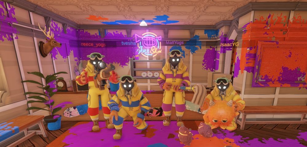 Screenshot from Monster Mop Up of the Yogscast Games team in a level. They are in yellow jumpsuits, one has a gun, another is kneeling, another has a mop, and the last one is holding an orange fluffy monster.