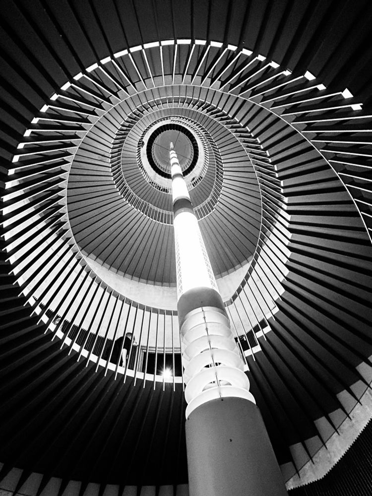Black and white image looking up from the bottom of a spiral staircase. 