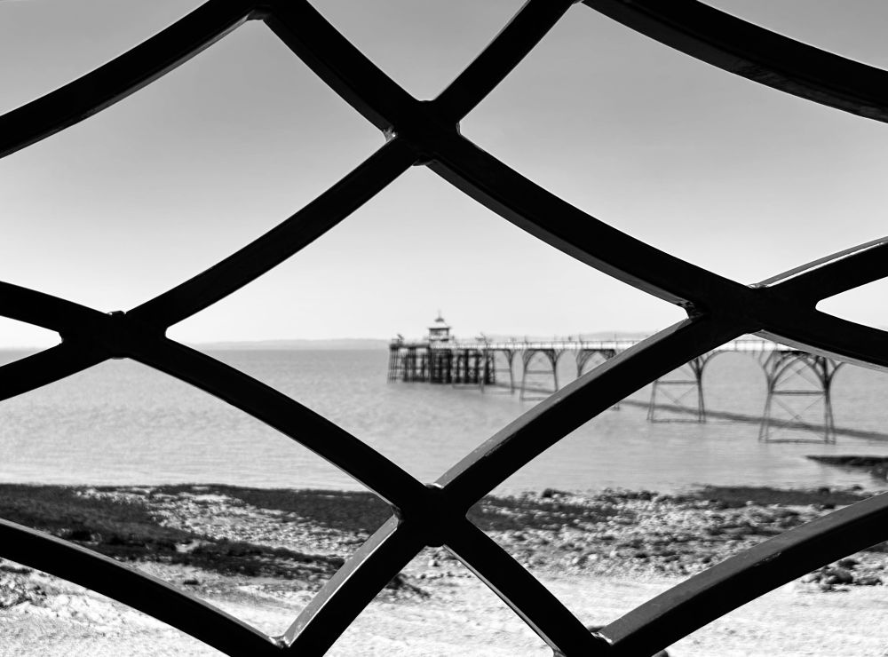 Black and white view of a pier, from looking through a gap in the x-shaped railings.