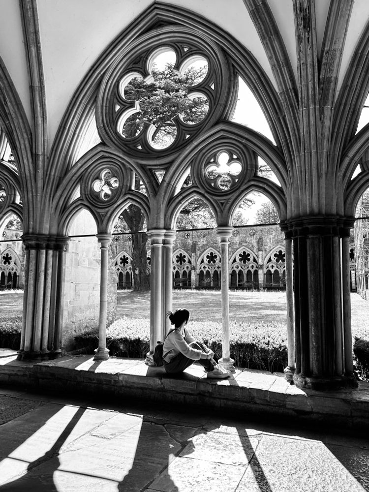A girl sitting beside the shadowy arched windows of the cloisters. 