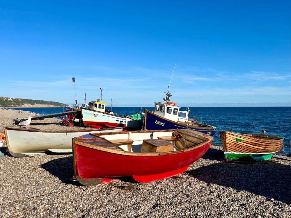 Boats resting on a shingle beach with blue sky and sea n the background. 