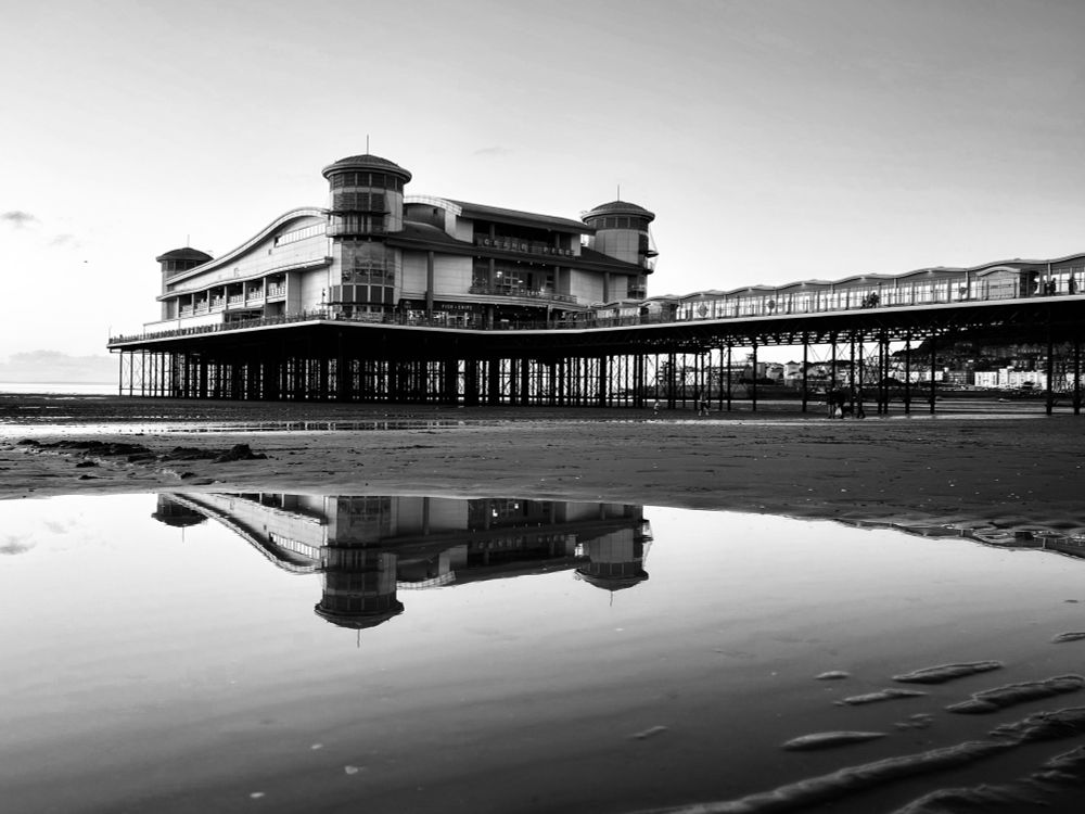 Black and white image of the Grand Pier, and the reflection in a rock pool at low tide. 