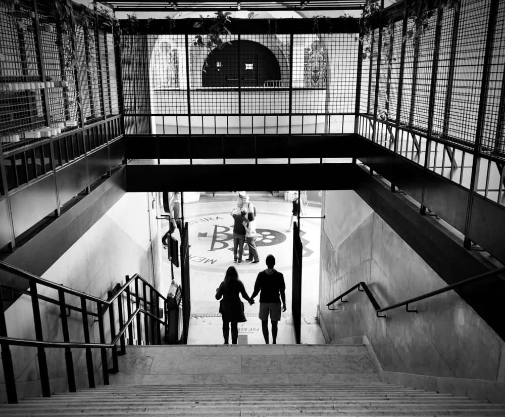 A silhouetted couple holding hands at the bottom of steps walking towards a light entrance. 