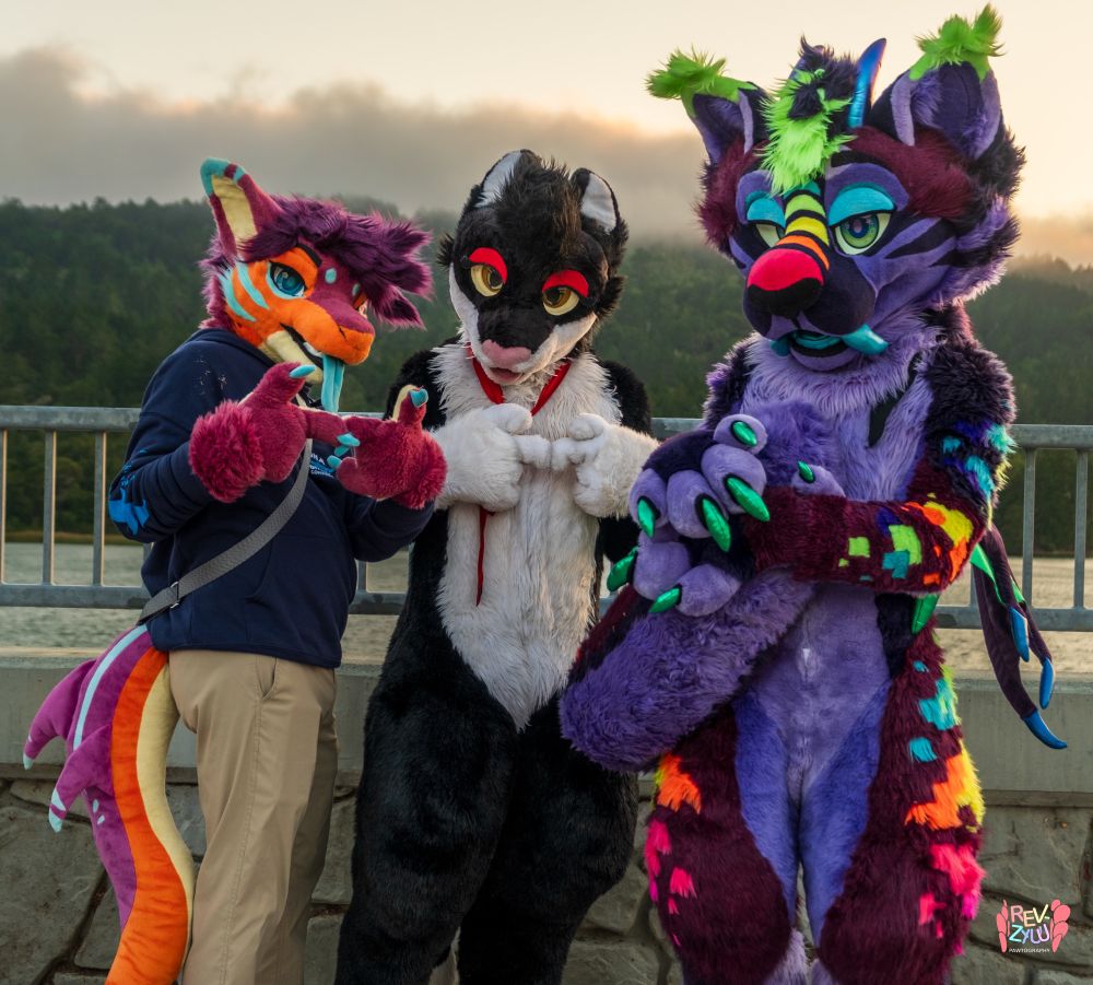Starburst and Jamie giving a finger-tapping gesture as Streak holds his tail. Trees and a river are visible behind a railing in the background