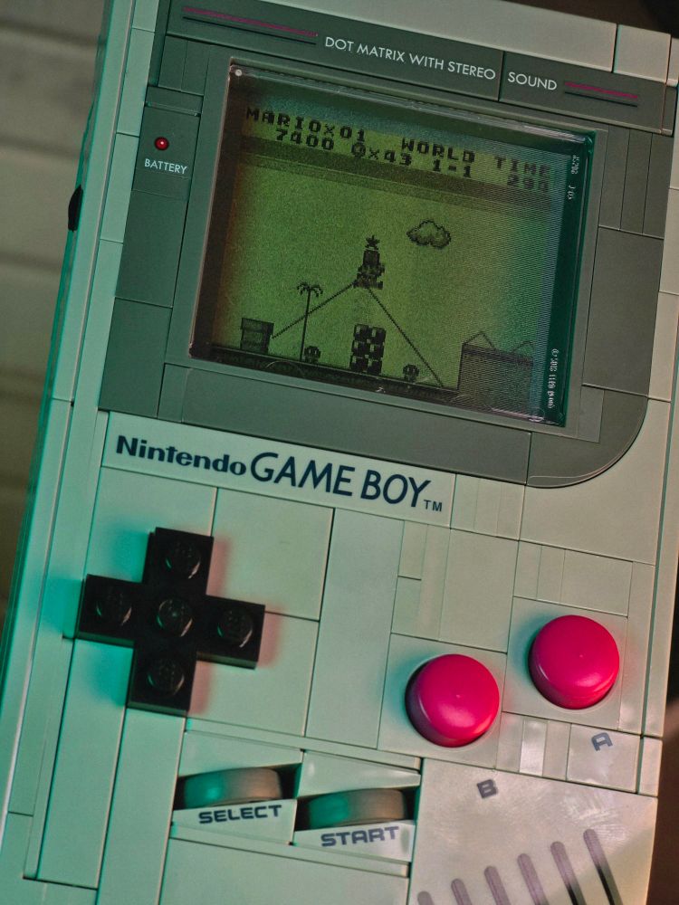 A photo of the Lego Game Boy. The screen shows a scene from Super Mario Land, of Mario in World 1-1 jumping to get a star out of an overhead item block.